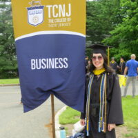 TCNJ student next to the business sign