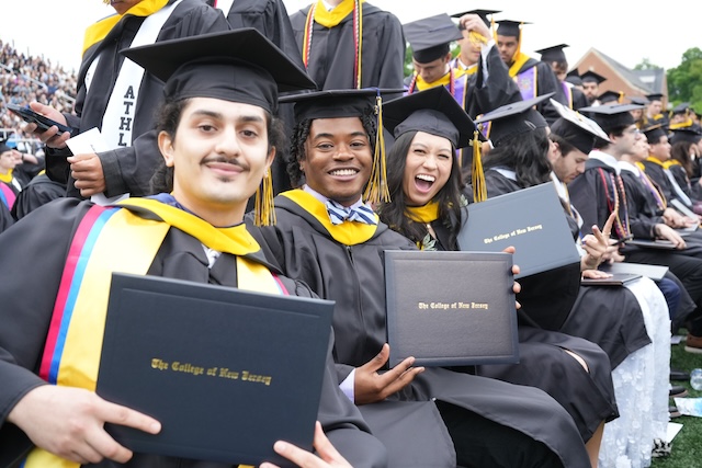 three grads in caps and gowns hold their diploma covers